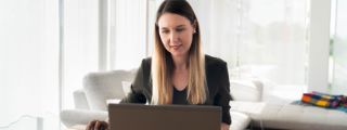 Eine Frau arbeitet konzentriert an einem Laptop in einer neutralen Home-Office-Umgebung.